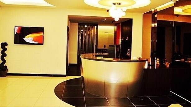 A reception area with a curved counter, a television mounted on the wall, and a chandelier. - Goldenhill Hotel (Kota Kinabalu)