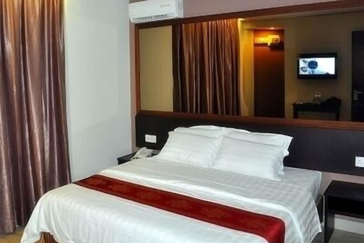 A hotel room with a large bed, a flat-screen TV mounted on the wall, and a window with curtains.