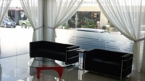 A modern hotel lobby with a glass partition, a red and black chair, and a car visible through the window. - Goldenhill Hotel (Kota Kinabalu)