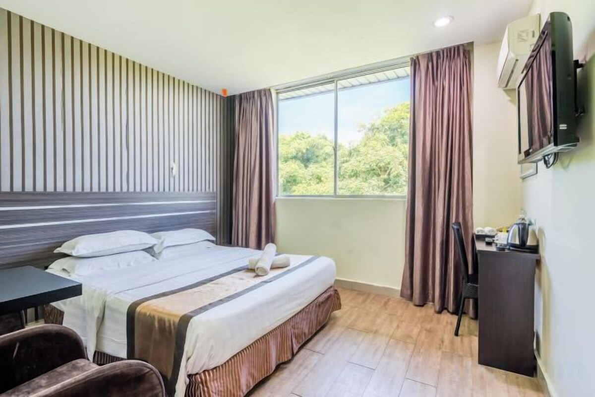 A hotel room with a bed, desk, chair, and a window with curtains.
