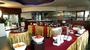 Un buffet avec différents postes de service proposant une variété de plats, notamment un présentoir de fruits, un coin café et un bar à salades.