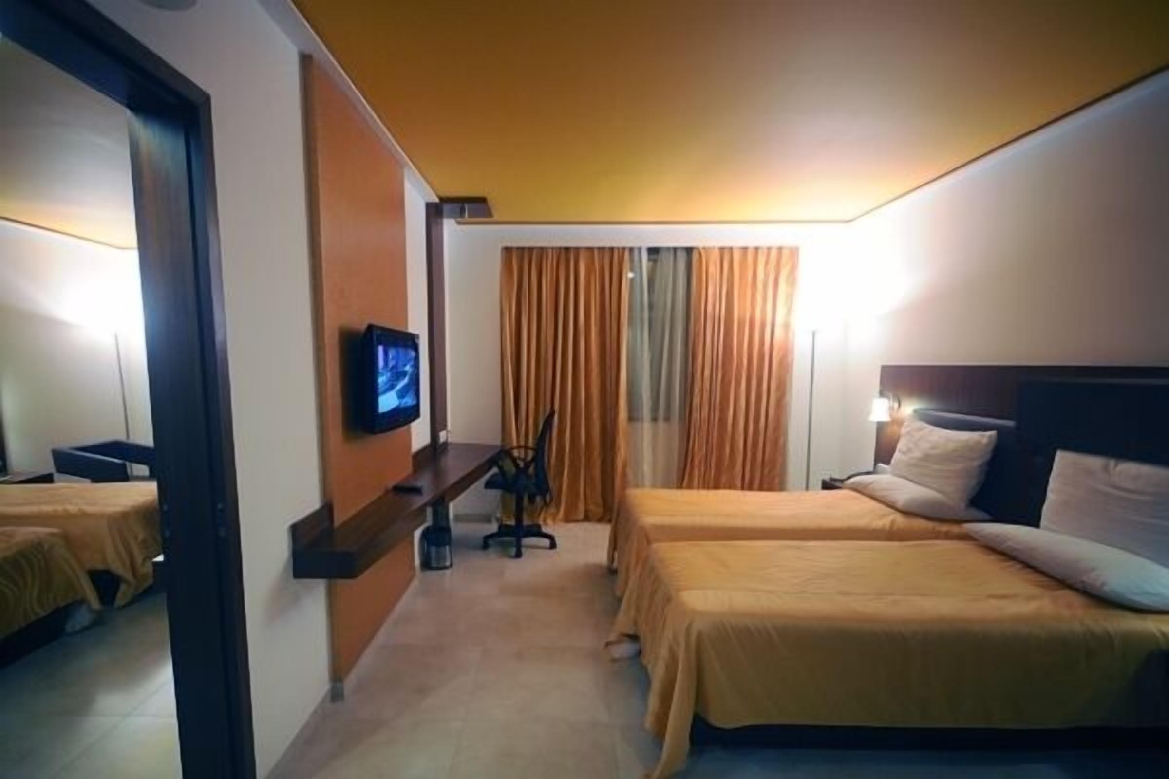 Een hotelkamer met twee bedden, een bureau, een televisie en gordijnen.
