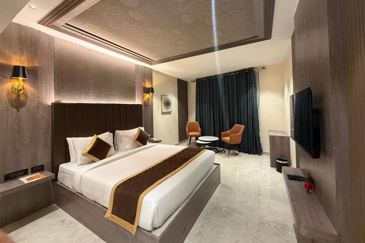 Una habitación de hotel moderna con una cama grande, dos sillones, una mesita, un televisor y un techo con un diseño floral.