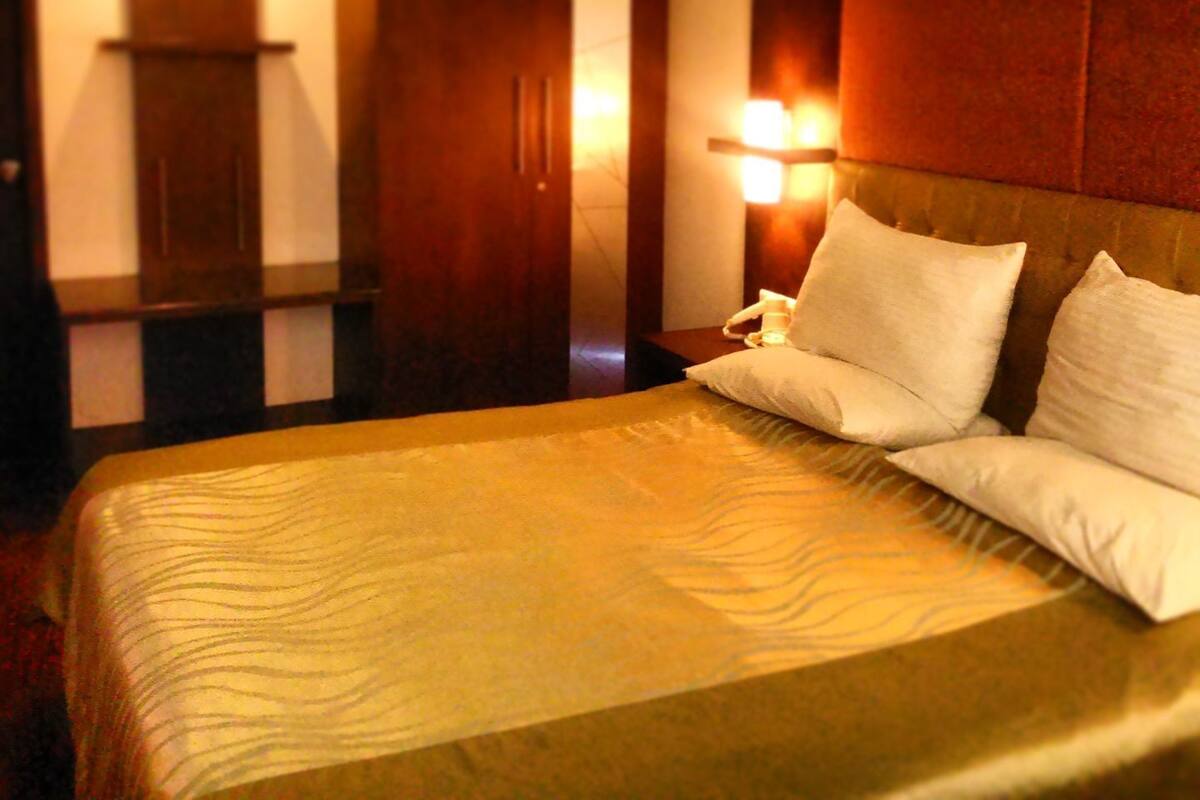 Una habitación de hotel con una cama grande, un armario de madera y una mesita de noche con lámpara.