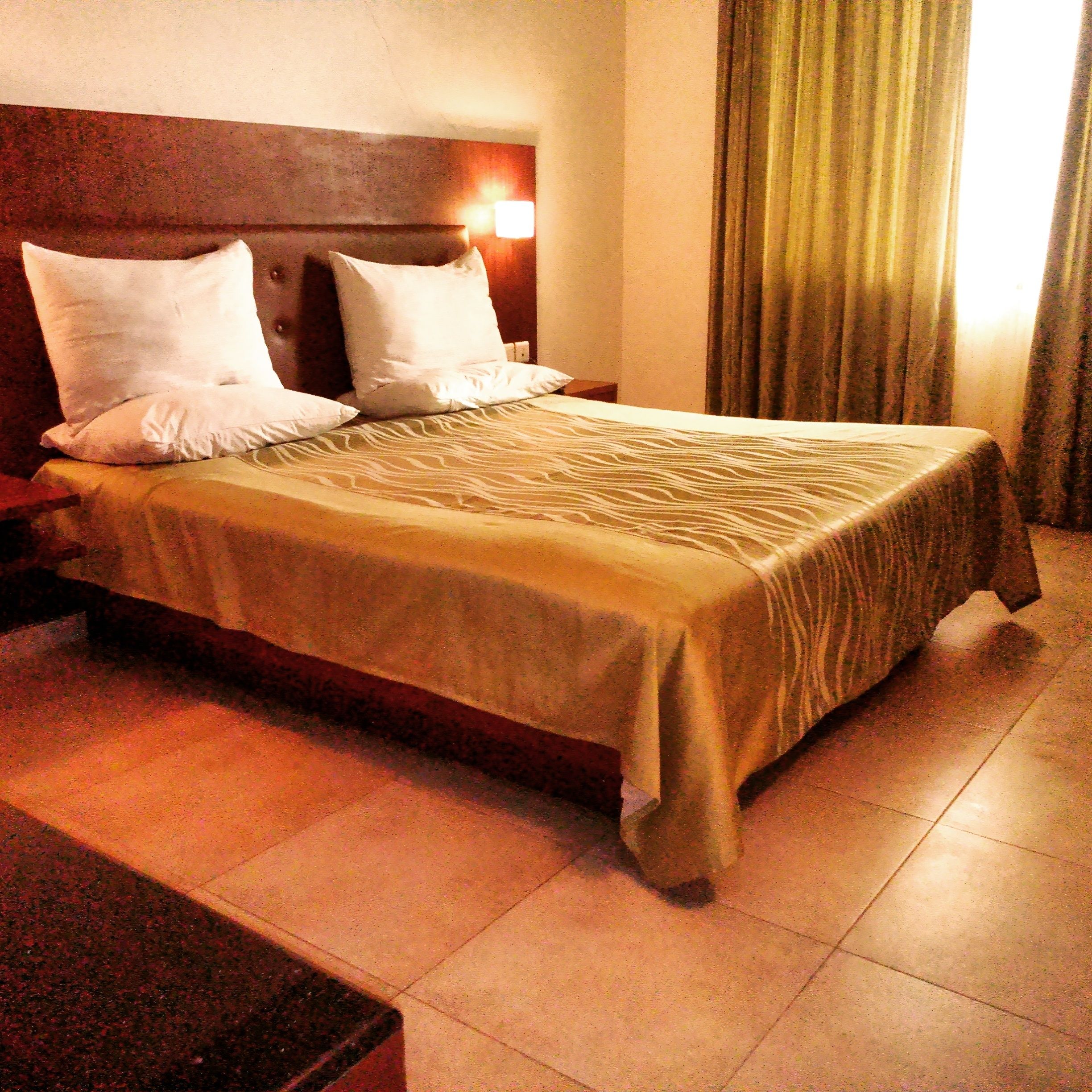 Una habitació d'hotel amb llit, tauletes de nit i capçalera amb llum.