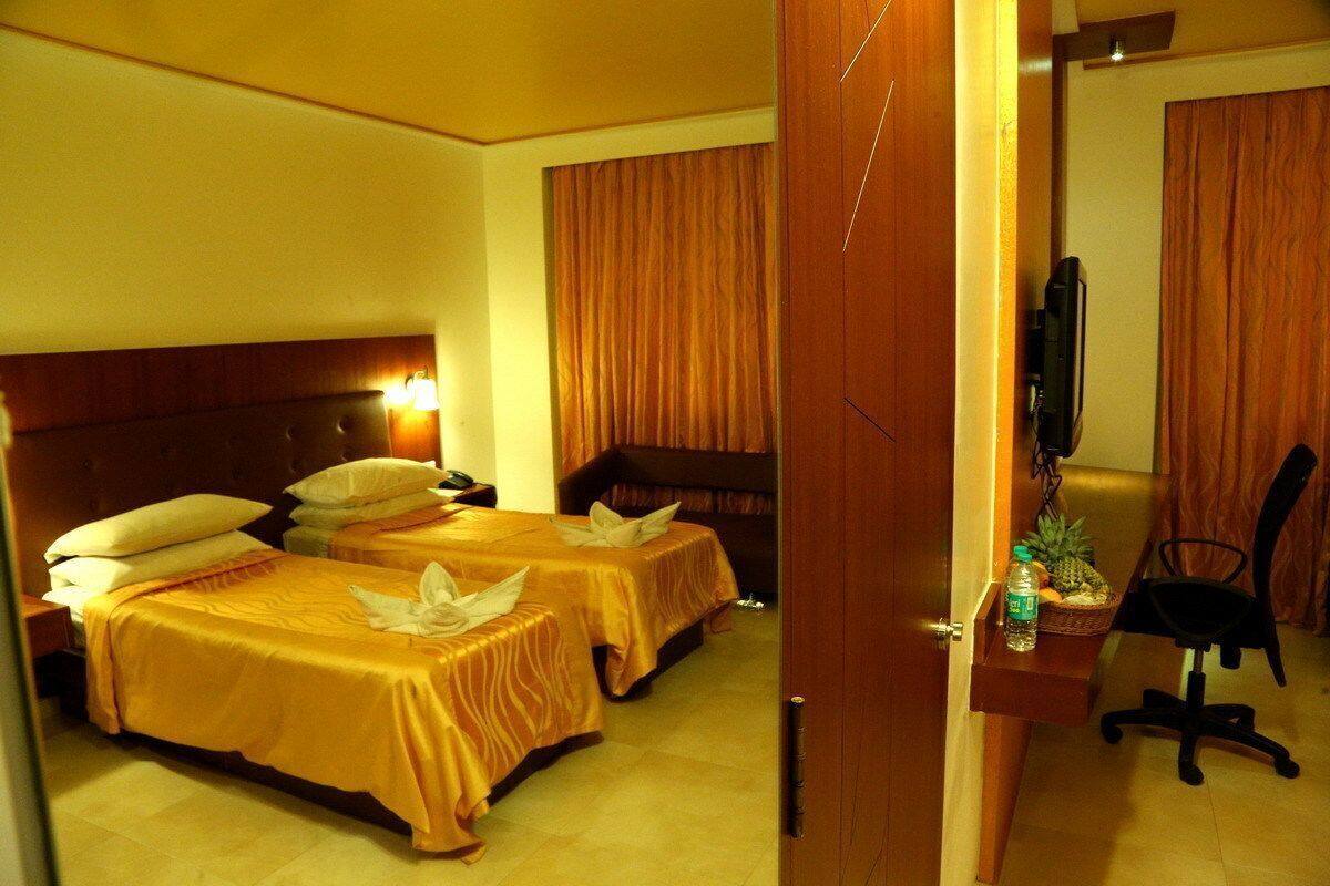 Habitación de hotel con dos camas, un escritorio con silla, televisor y una mesita con una botella y fruta.