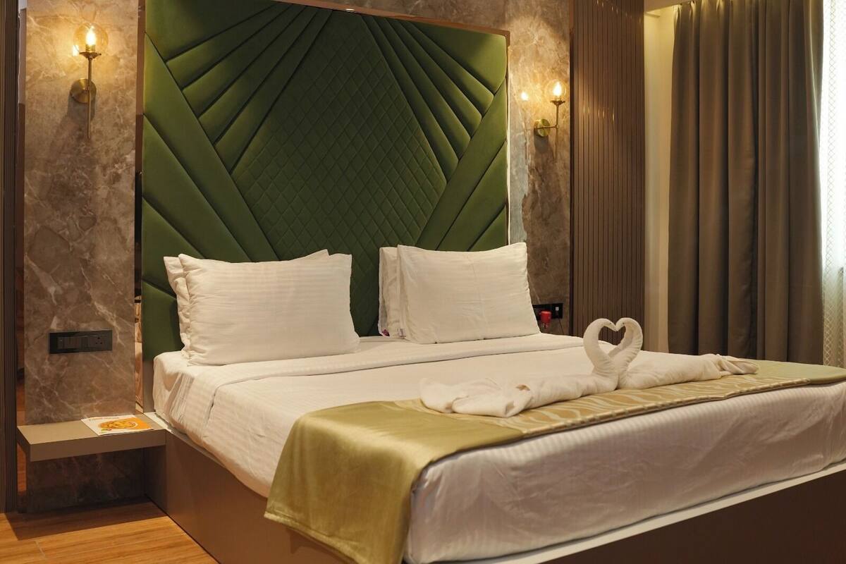 Una habitación de hotel con un cabecero tapizado en verde, una cama con ropa de cama blanca y toallas decorativas con forma de cisne.