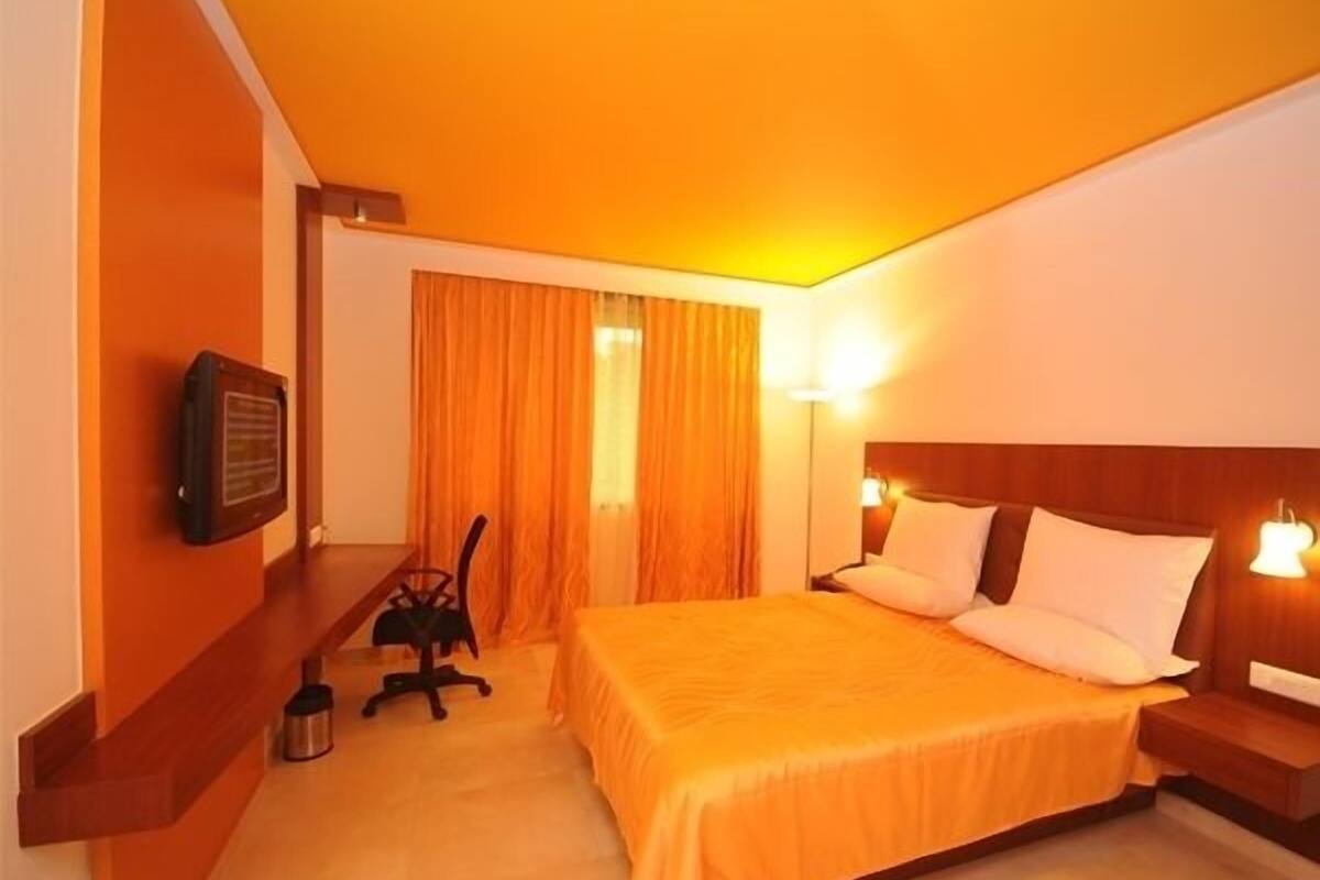 Una habitación de hotel con una cama, un escritorio, una silla, un televisor y una mesita de noche.
