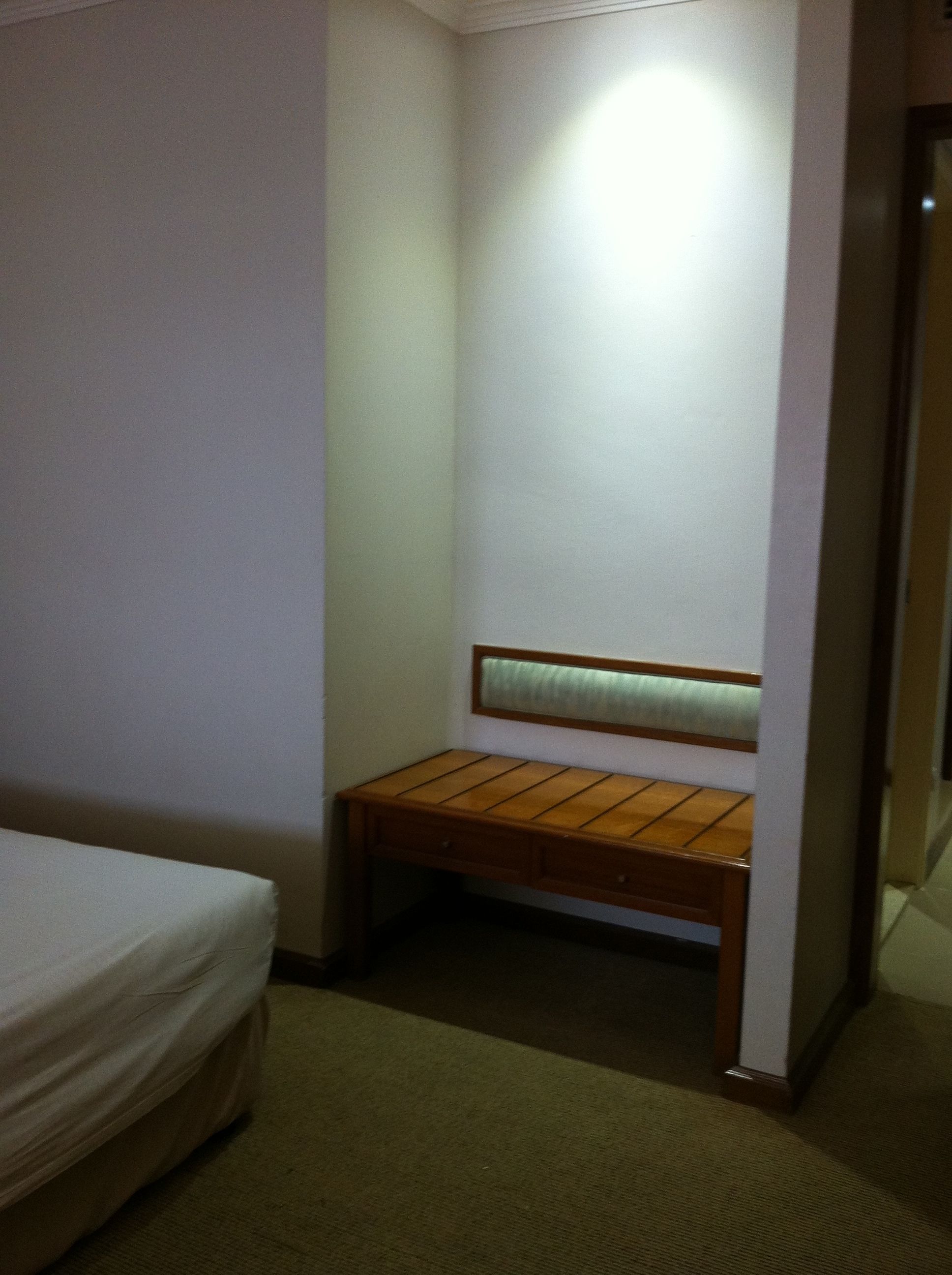 A small, dimly lit room with a single bed, a wooden bench, and a wall-mounted headboard.
