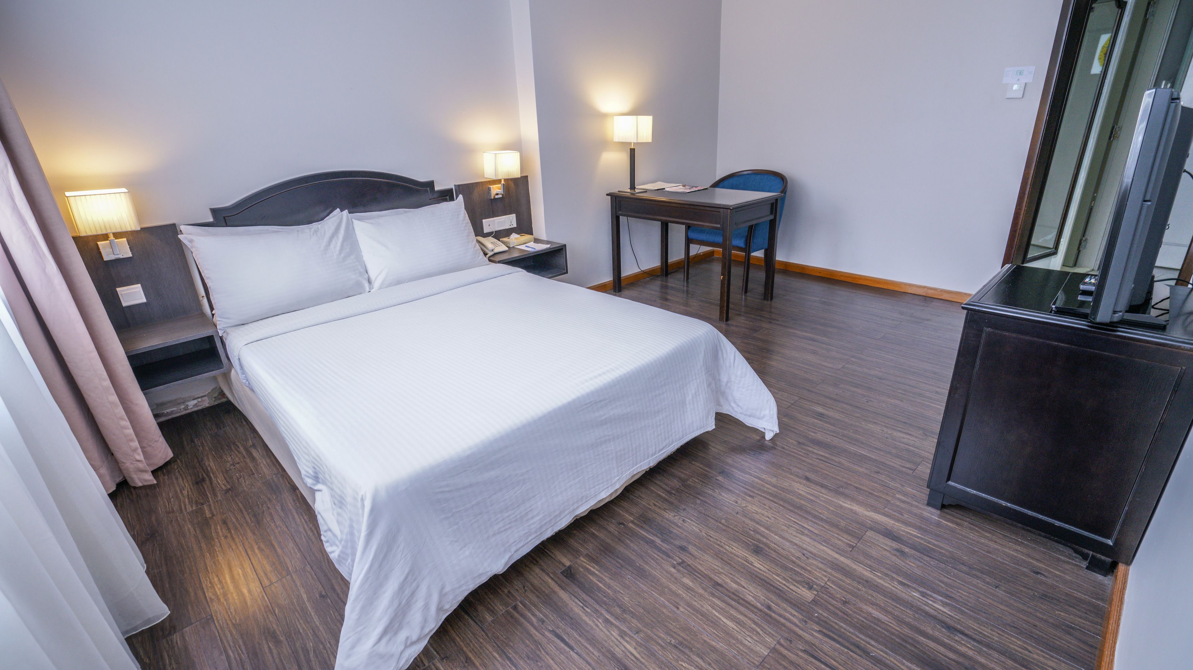 Una habitación de hotel con cama, lámparas de noche, escritorio, silla y televisor.