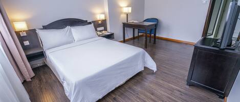 Una habitación de hotel con cama, lámparas de noche, escritorio, silla y televisor.