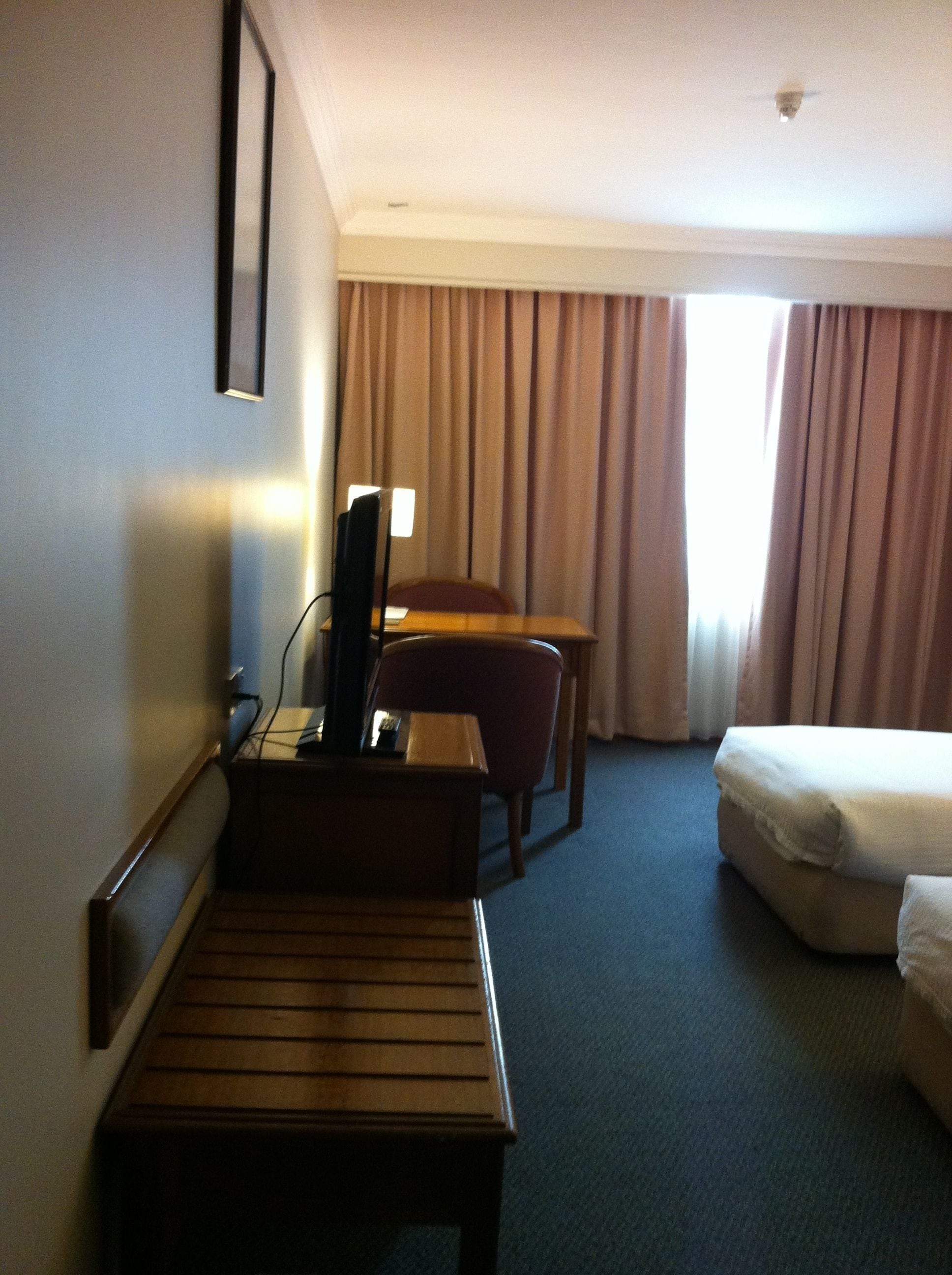 A hotel room with a bed, a desk with a computer, a chair, and a small table.