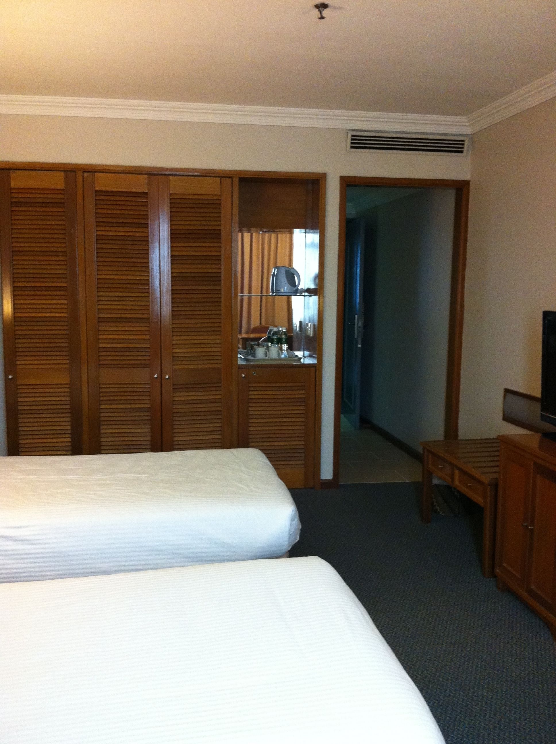 A hotel room with two beds, wooden wardrobes, a desk, and a television.