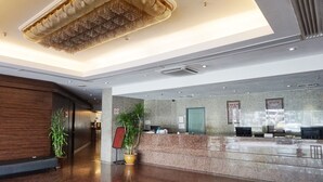 A modern hotel lobby with a reception desk, a large chandelier, and a potted plant. - Kingwood Hotel (Kuching)