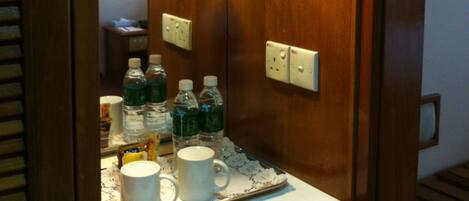 A compact kitchenette with a coffee maker, water bottles, and mugs on a tray.