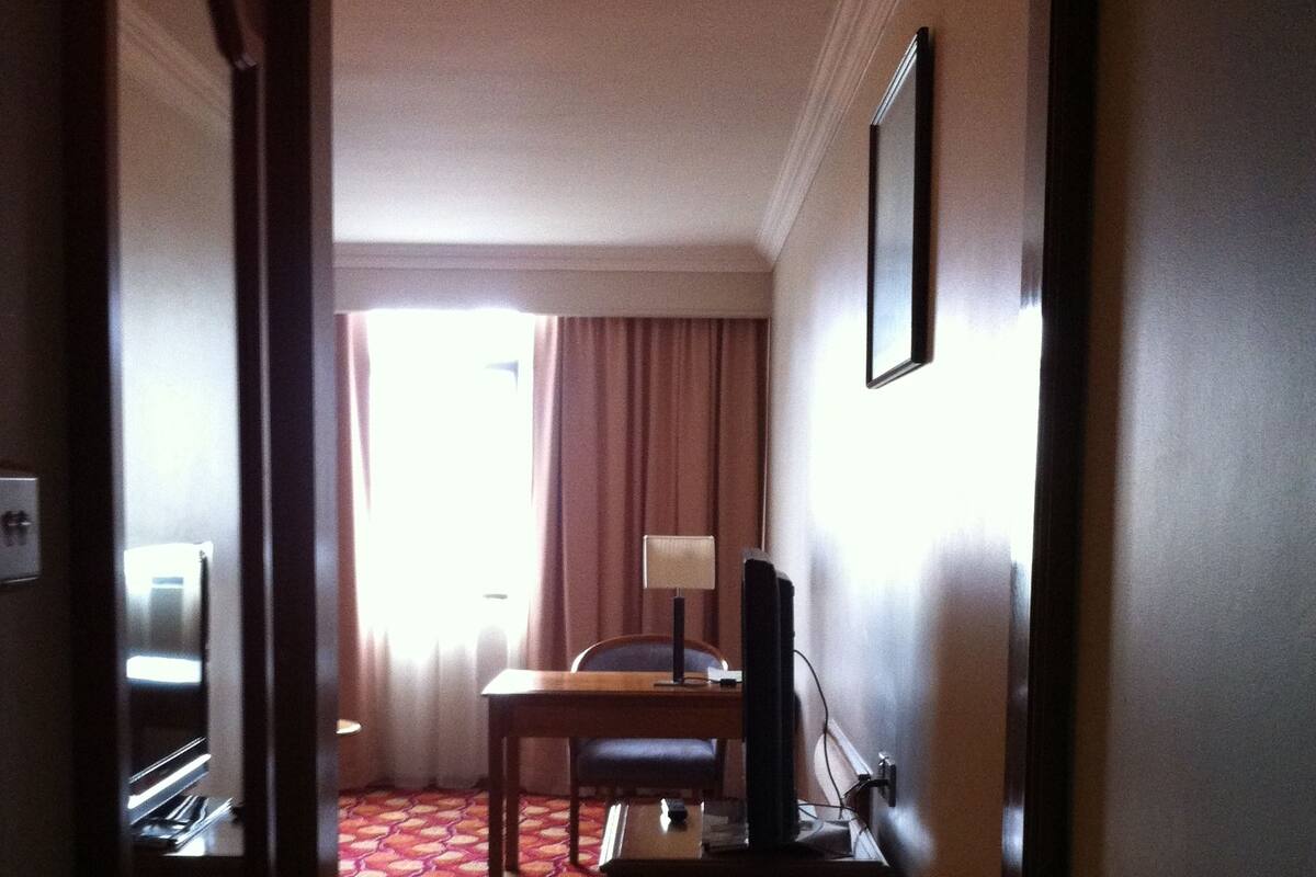 Habitación de hotel con alfombra de diseño rojo, un escritorio con silla, televisor y ventana con cortinas.