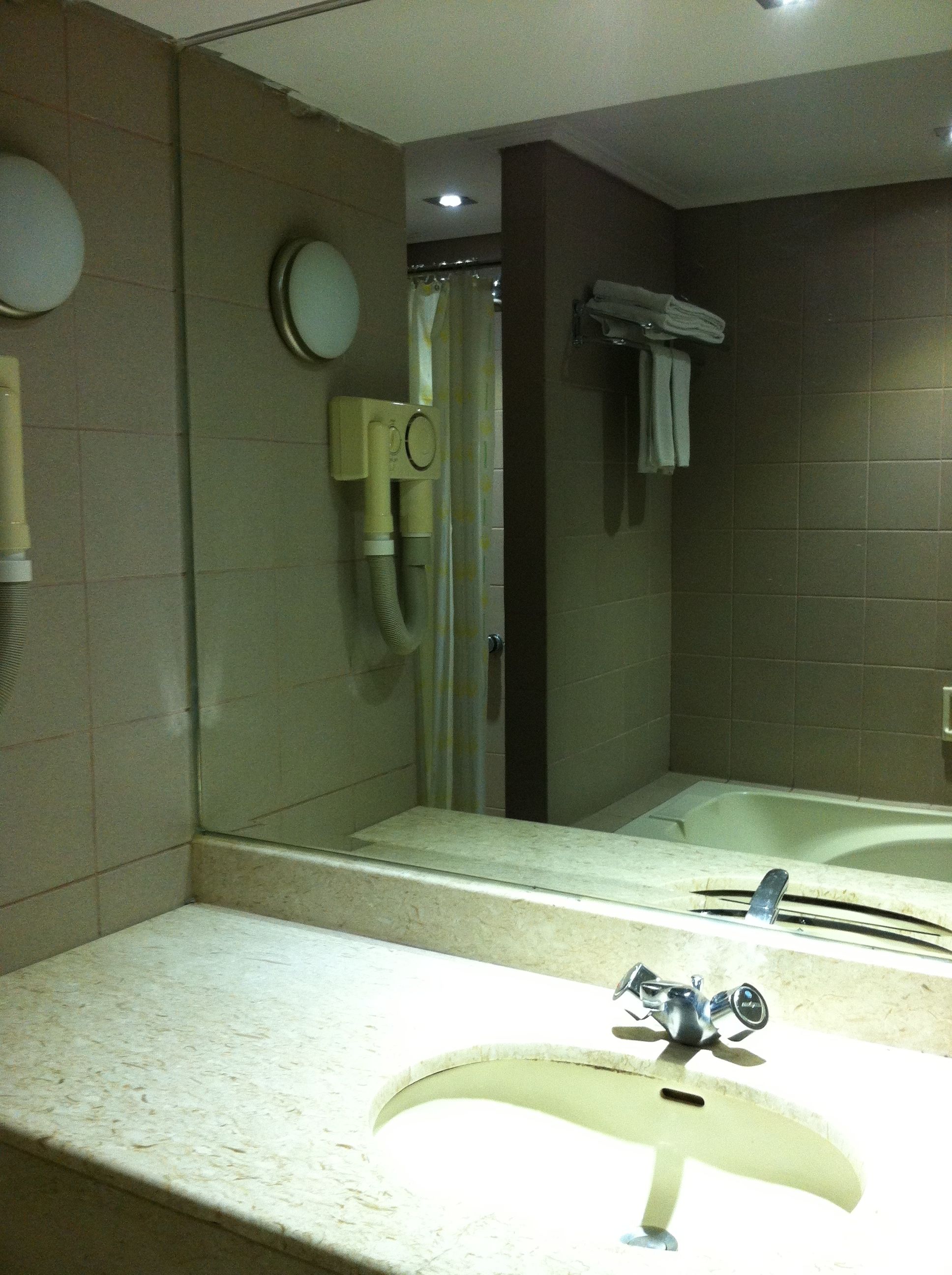 A bathroom with a sink, mirror, shower, and towel rack.