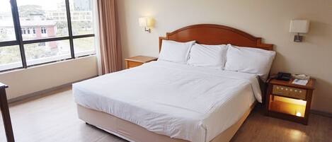 A hotel room with a large bed, two bedside tables, a nightstand, a window with curtains, and a painting on the wall.