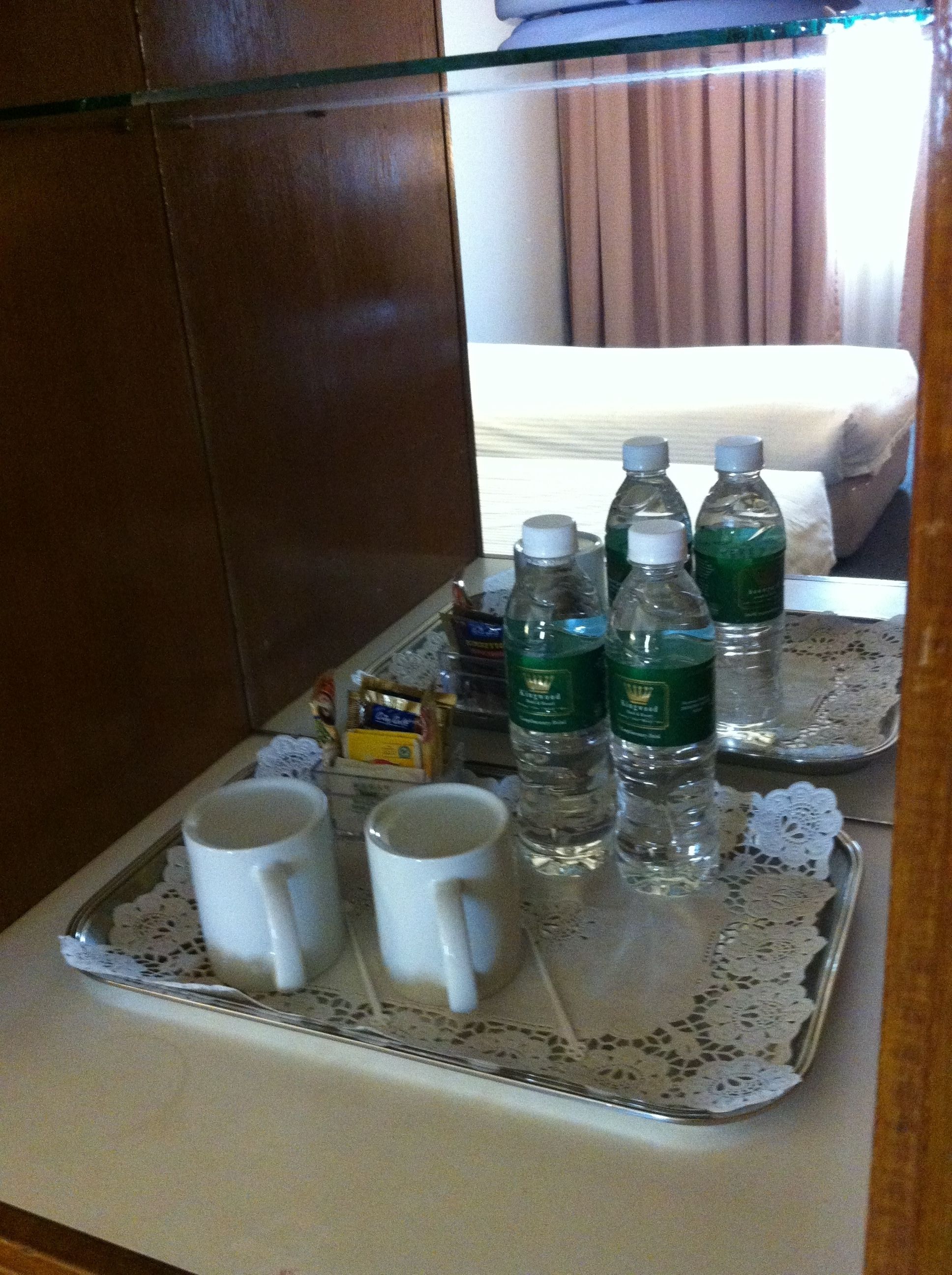 Una bandeja con dos tazas blancas, tres botellas de agua y una pequeña caja de pañuelos en una habitación de hotel.