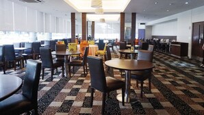 A modern hotel lobby with multiple dining areas, patterned carpet, and large windows allowing natural light. - Kingwood Hotel (Kuching)