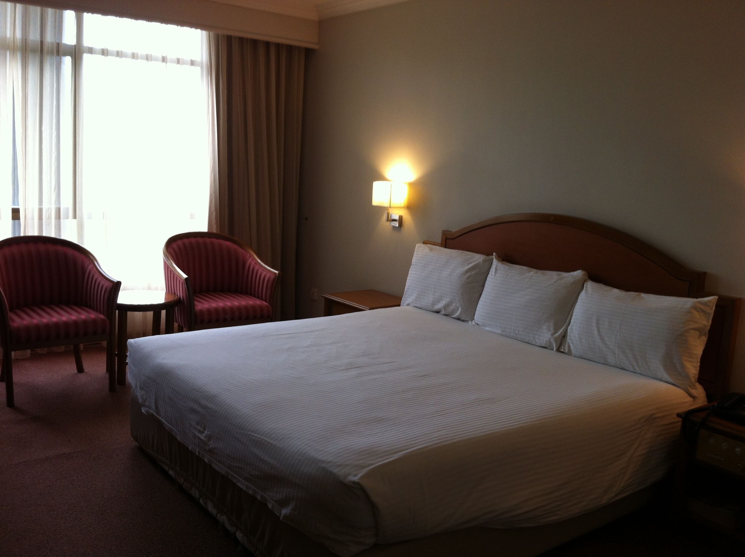A hotel room with a large bed, two red armchairs, a small table, and a nightstand.