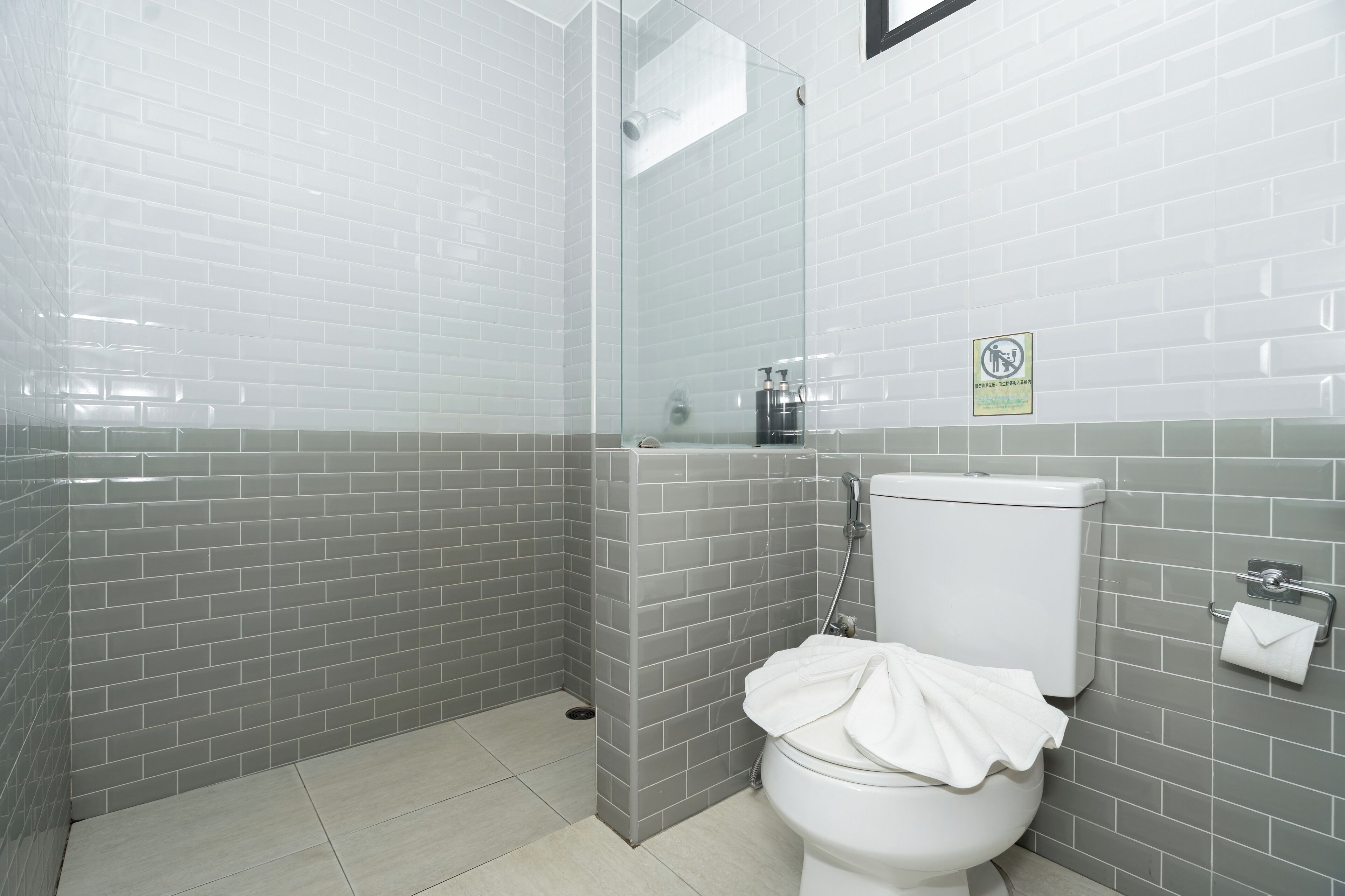 Ein Badezimmer mit grauen Fliesenwänden, einer Duschkabine aus Glas, einer Toilette und einem Handtrockner.