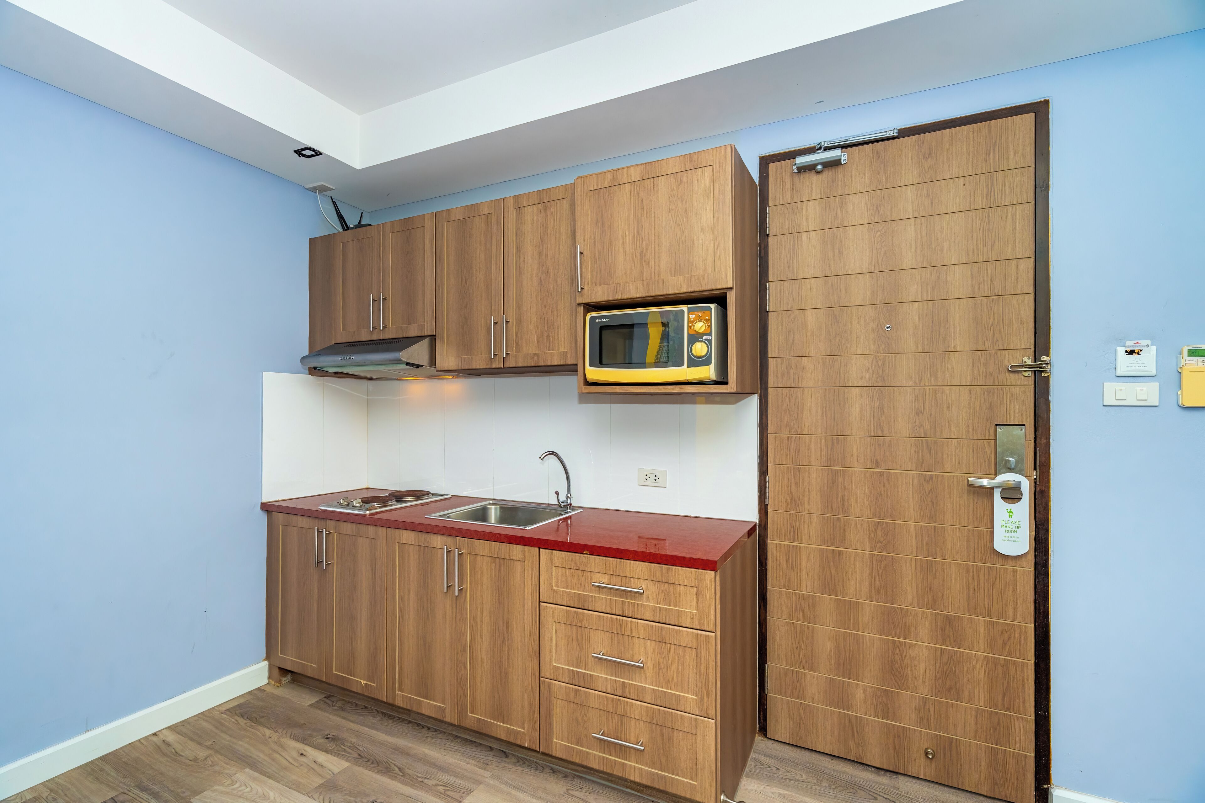 A compact kitchen with wooden cabinets, a microwave, a sink, and a door with a handle.