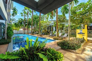 Une piscine entourée de palmiers et de chaises longues, avec un panneau jaune indiquant une profondeur de 1,45 mètre.