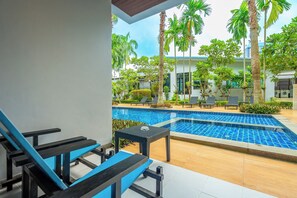 Un espace piscine avec des chaises longues, une petite table et des palmiers.