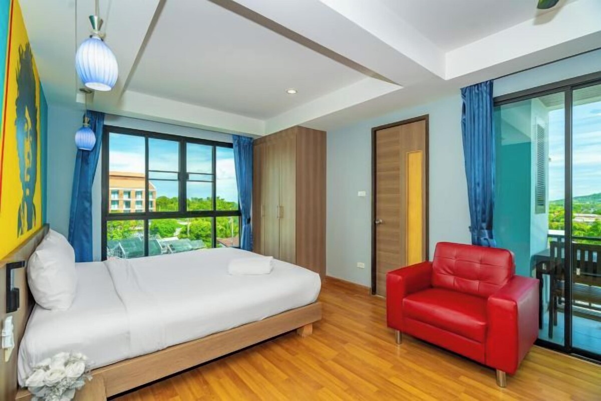 A modern bedroom with a wooden bed, a red leather chair, large windows, and a view of the outdoors.