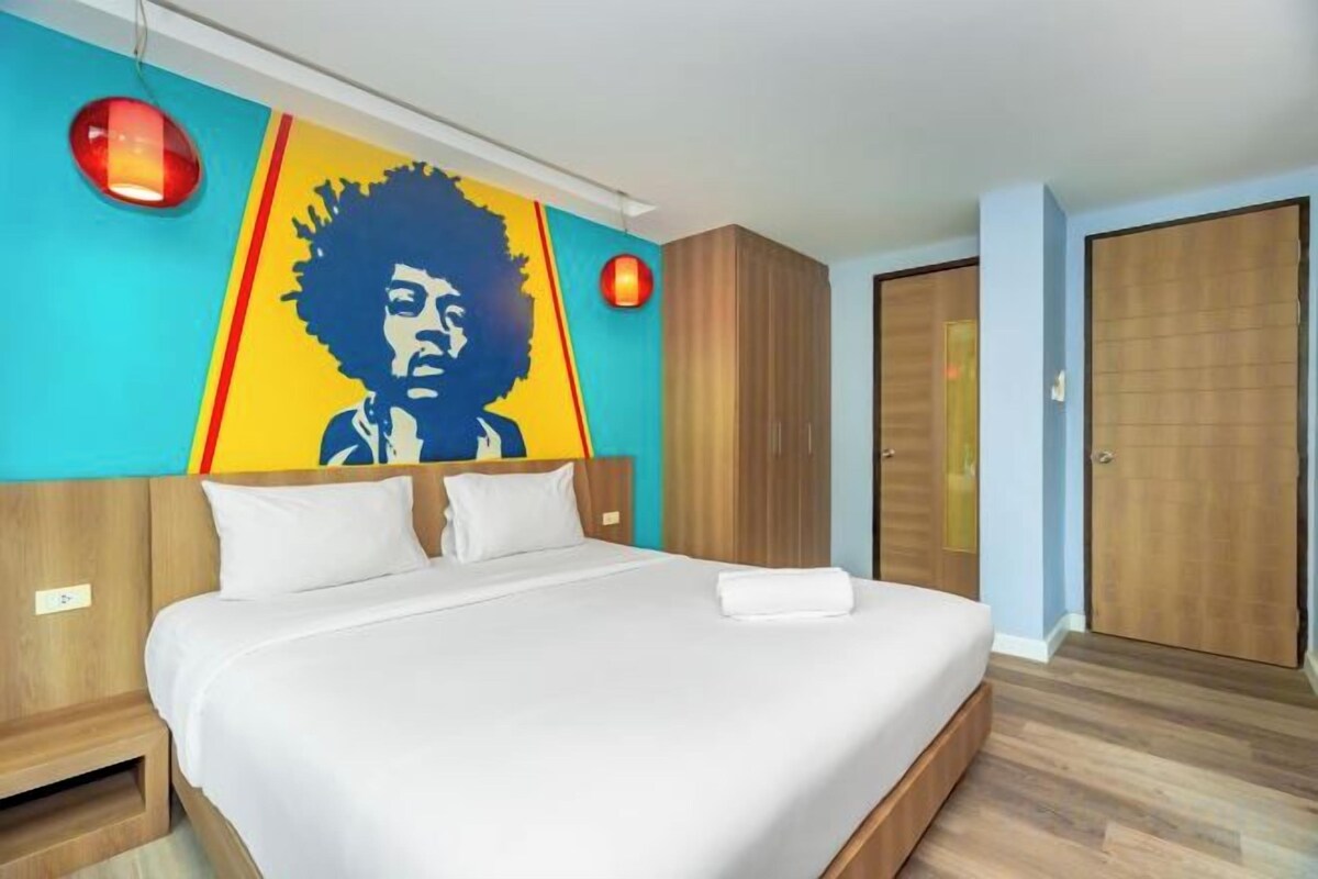 Une chambre d’hôtel avec un grand lit, une armoire et un mur orné d’une fresque colorée.