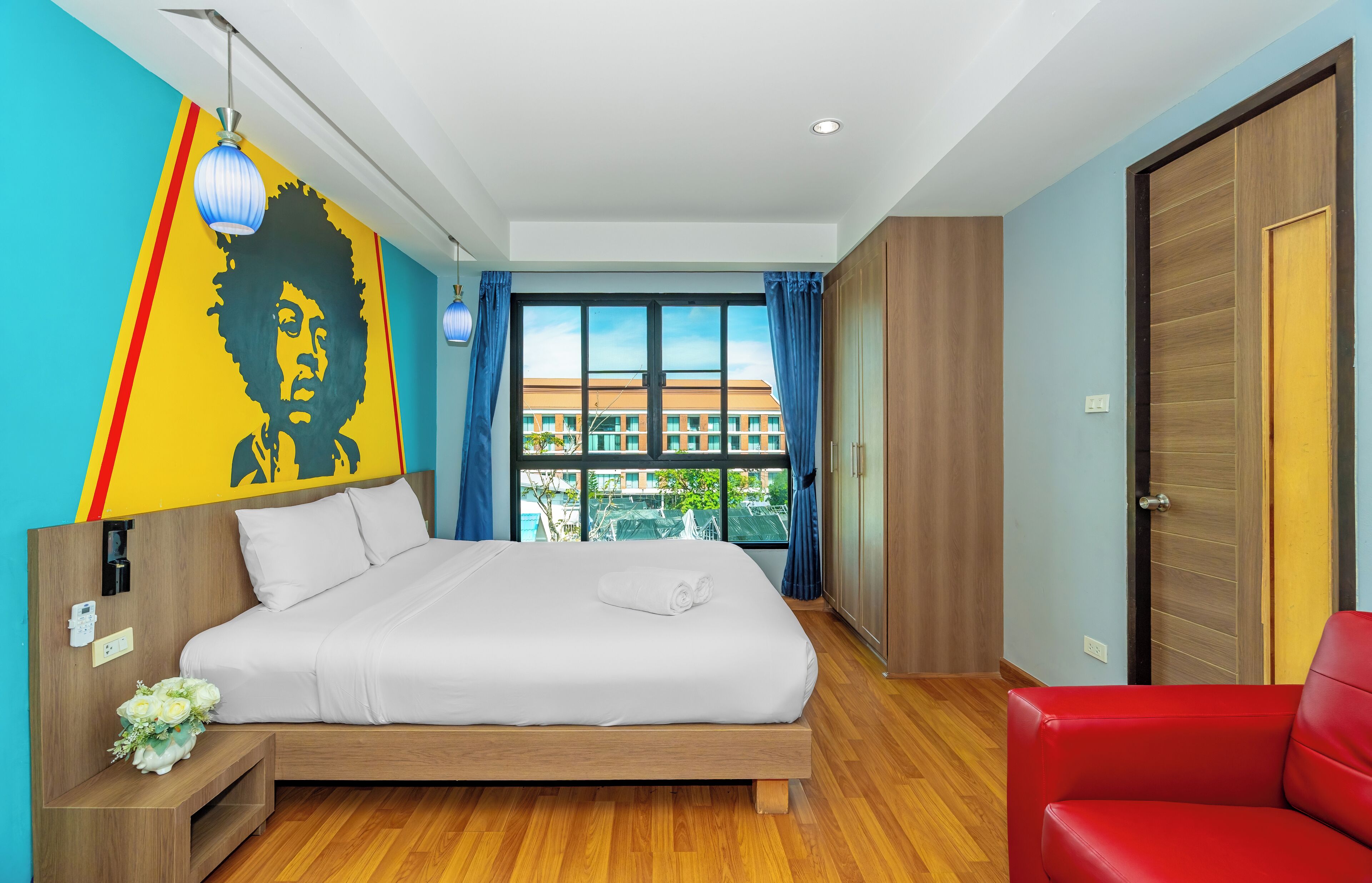Una habitación de hotel moderna con una cama grande, una silla roja y vistas a edificios a través de la ventana.