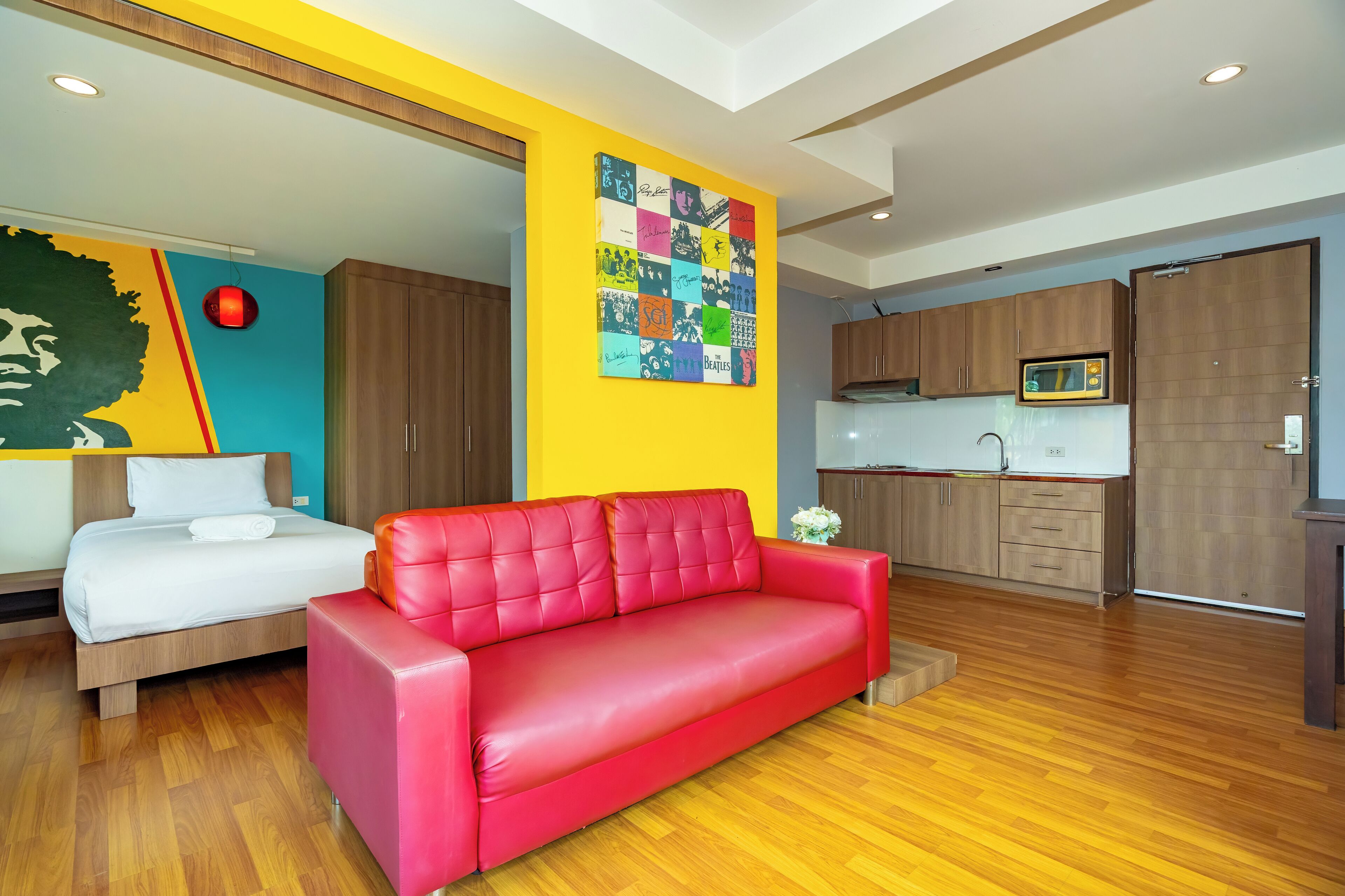 A modern living room with a red sofa, a bed, and a colorful wall art piece.