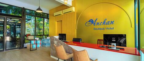 A reception desk with a yellow wall and a sign that reads "Anchan Boutique Hotel".