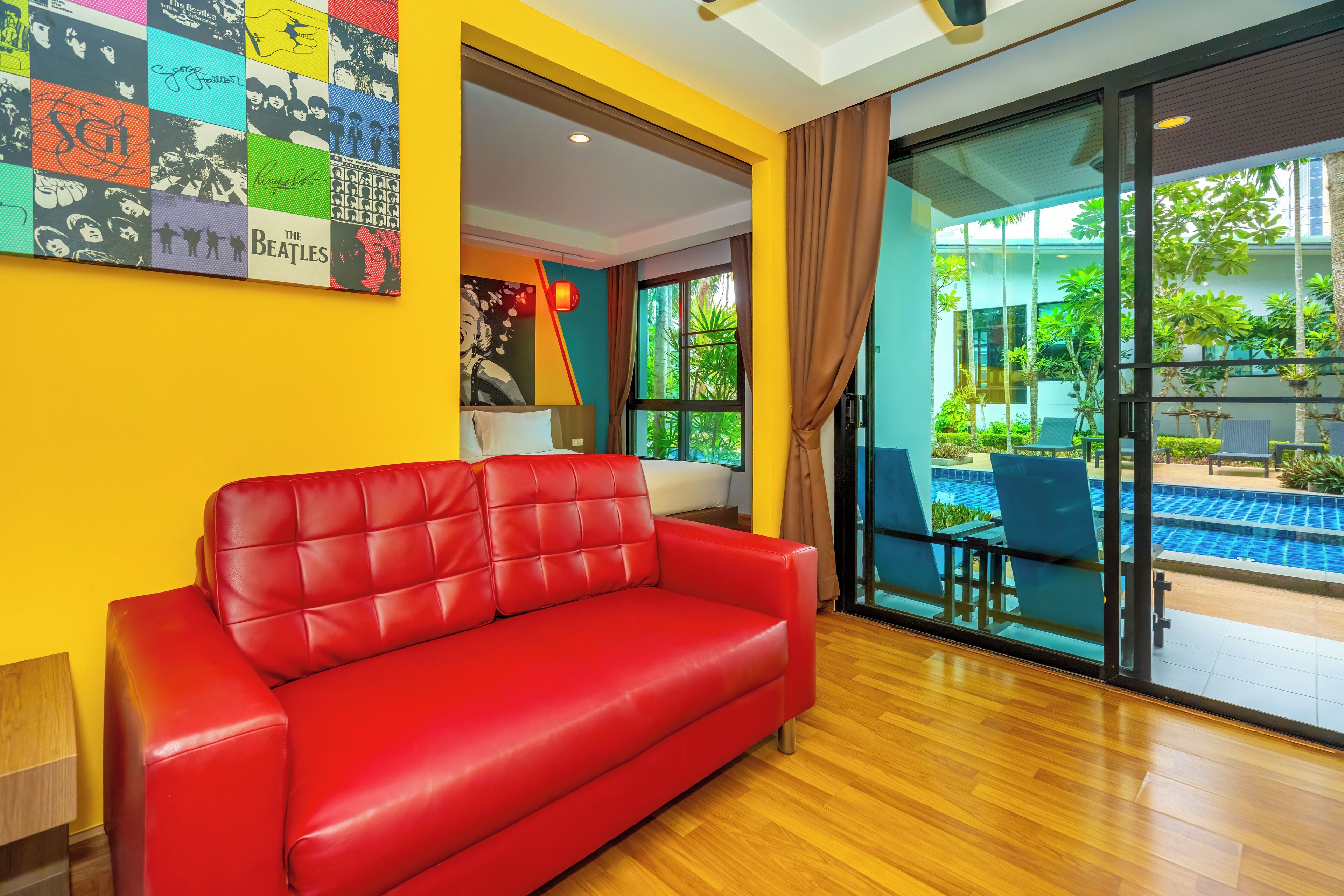 A modern living room with a red sofa, a colorful wall art piece, and a view of an outdoor swimming pool.