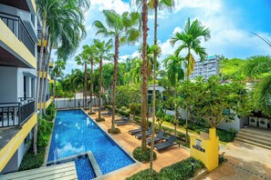 A swimming pool with lounge chairs, surrounded by palm trees and a building with balconies.