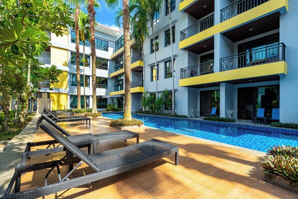 A modern hotel with a swimming pool, lounge chairs, and a well-maintained garden.