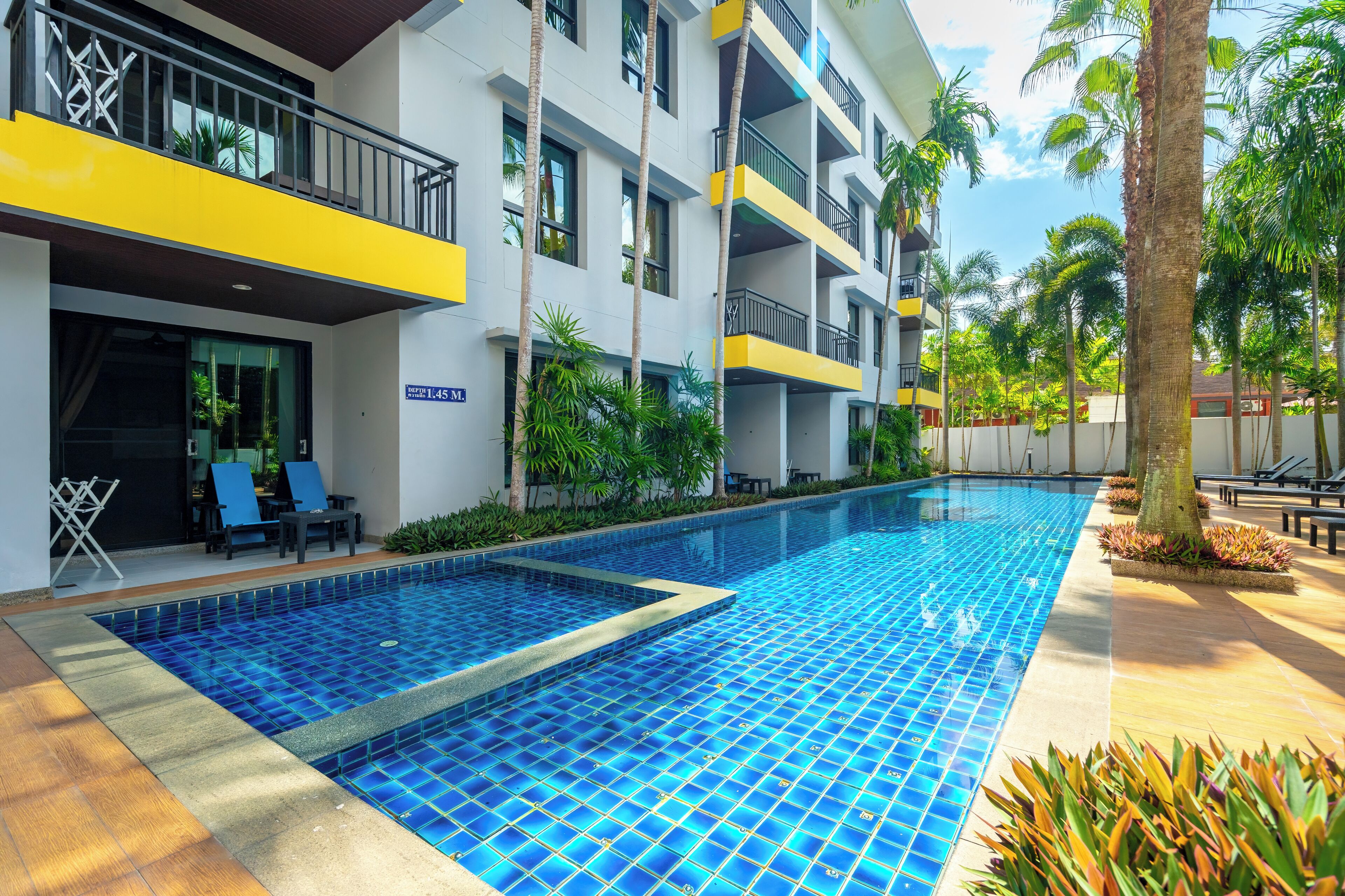 Un hotel moderno con piscina, varios balcones y abundante vegetación.
