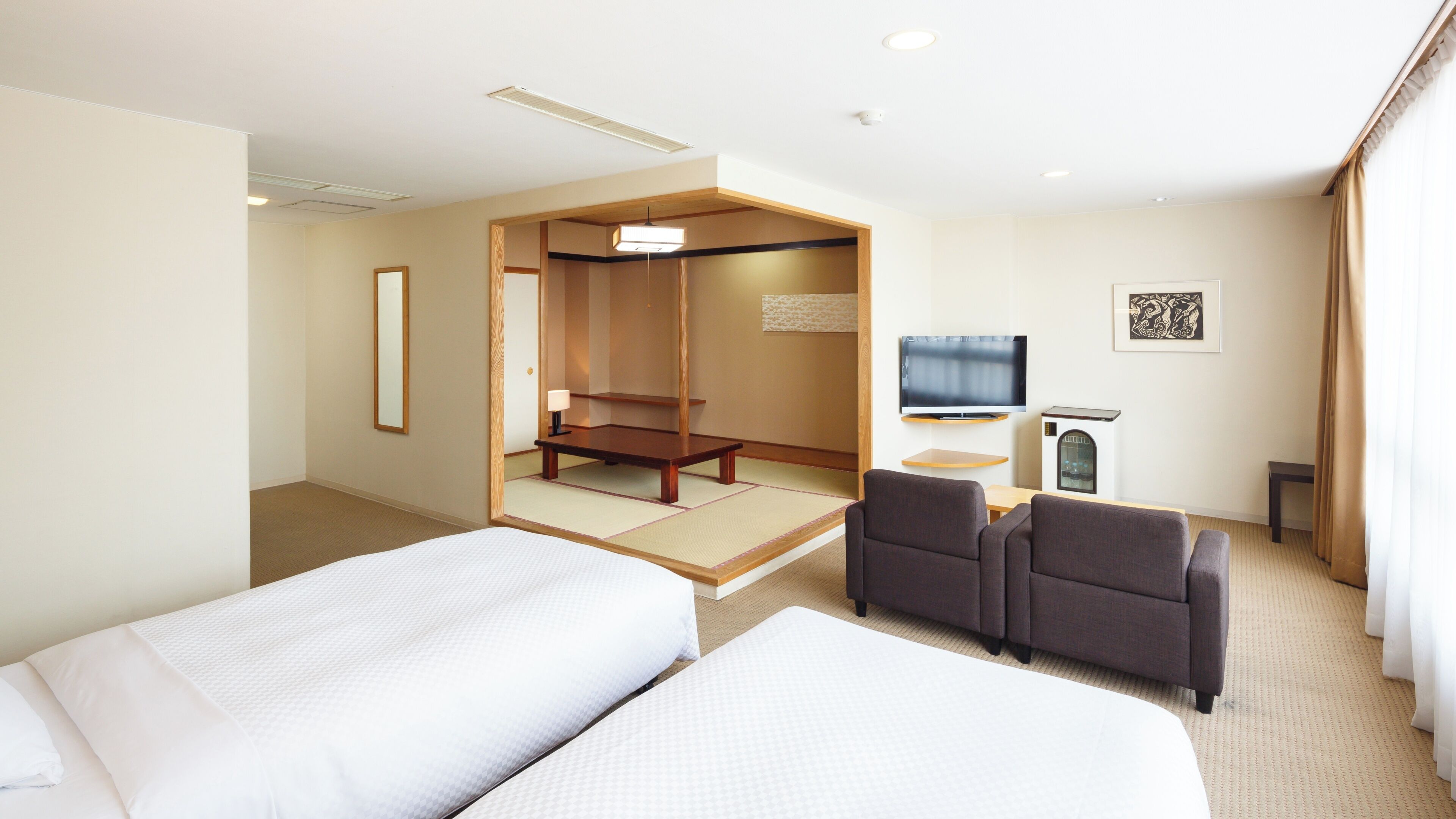 Quarto de hotel com duas camas, área de estar com sofá, televisão e um divisória de ambiente tradicional japonesa.