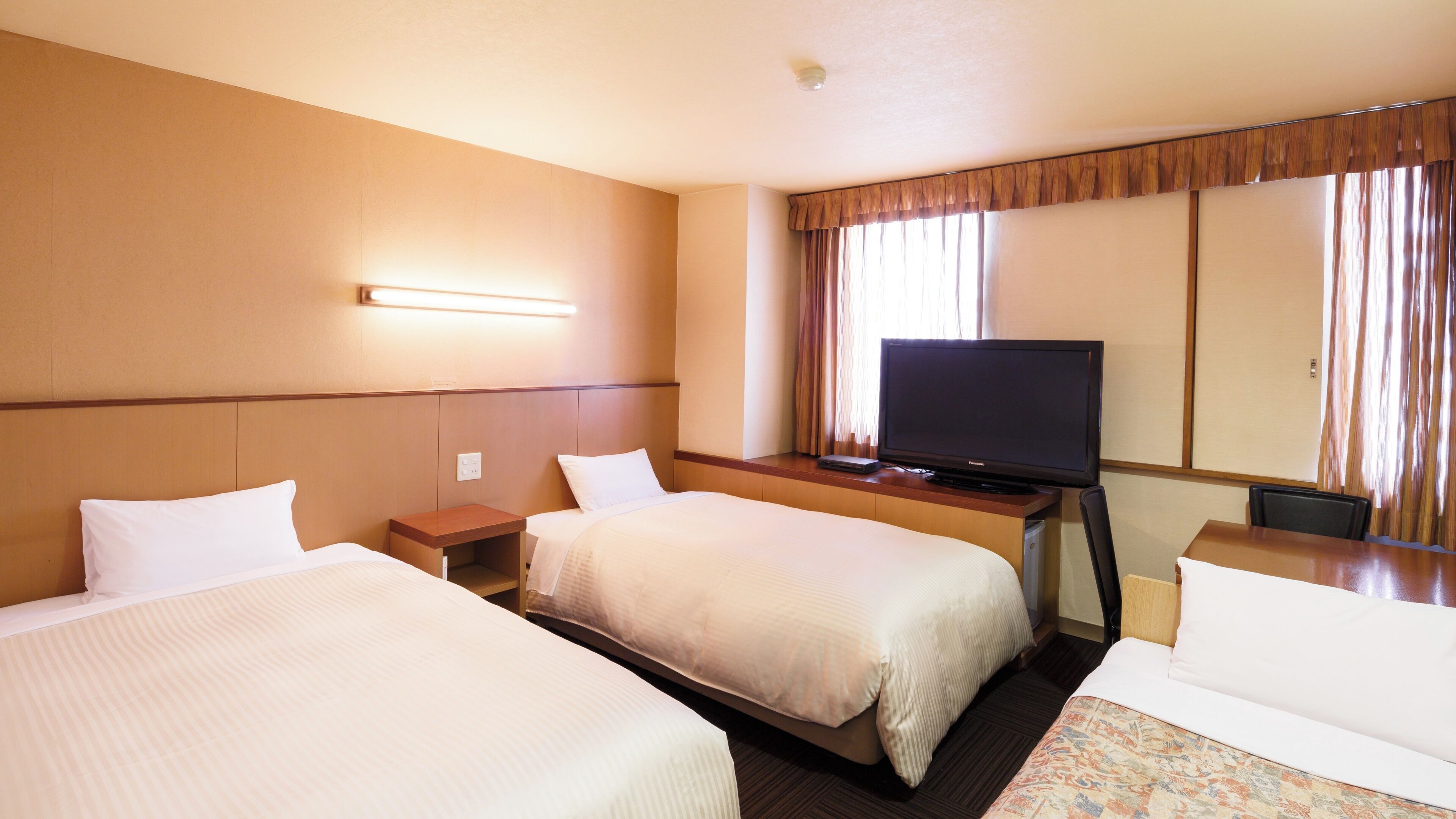 Quarto de hotel com duas camas, televisão, escrivaninha e janela com cortinas.