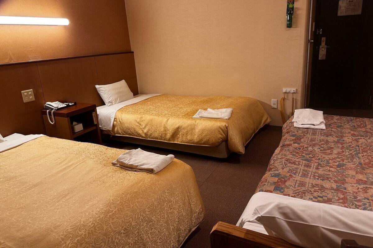 Una habitación de hotel con dos camas, una mesita de noche con teléfono e iluminación en la pared.