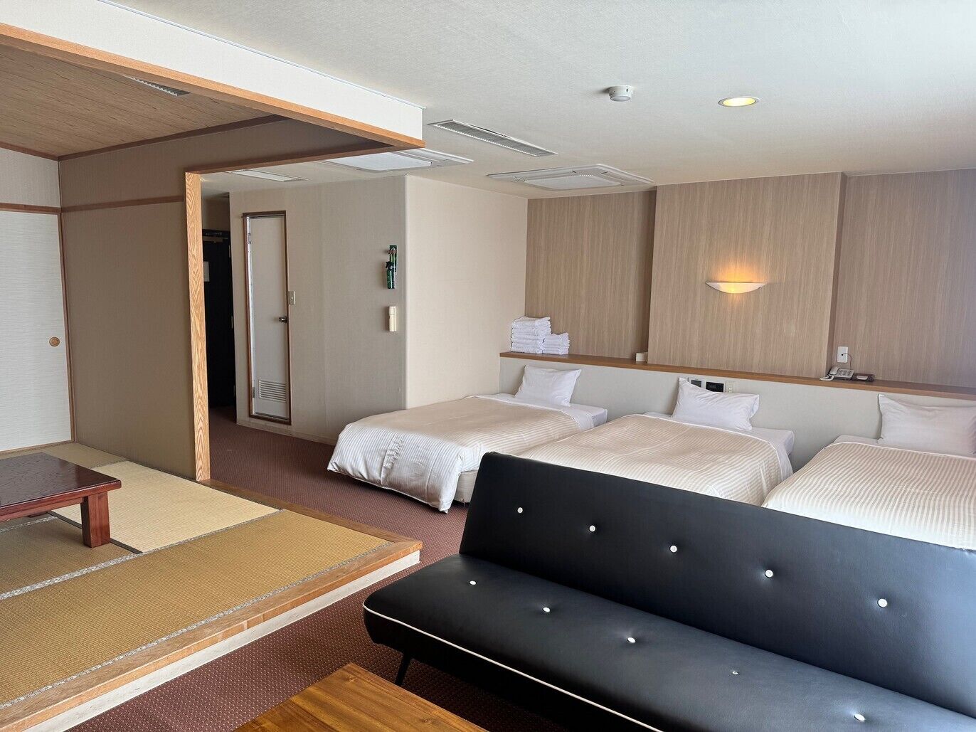 Quarto de hotel com duas camas, um sofá, uma mesa pequena e um espelho.