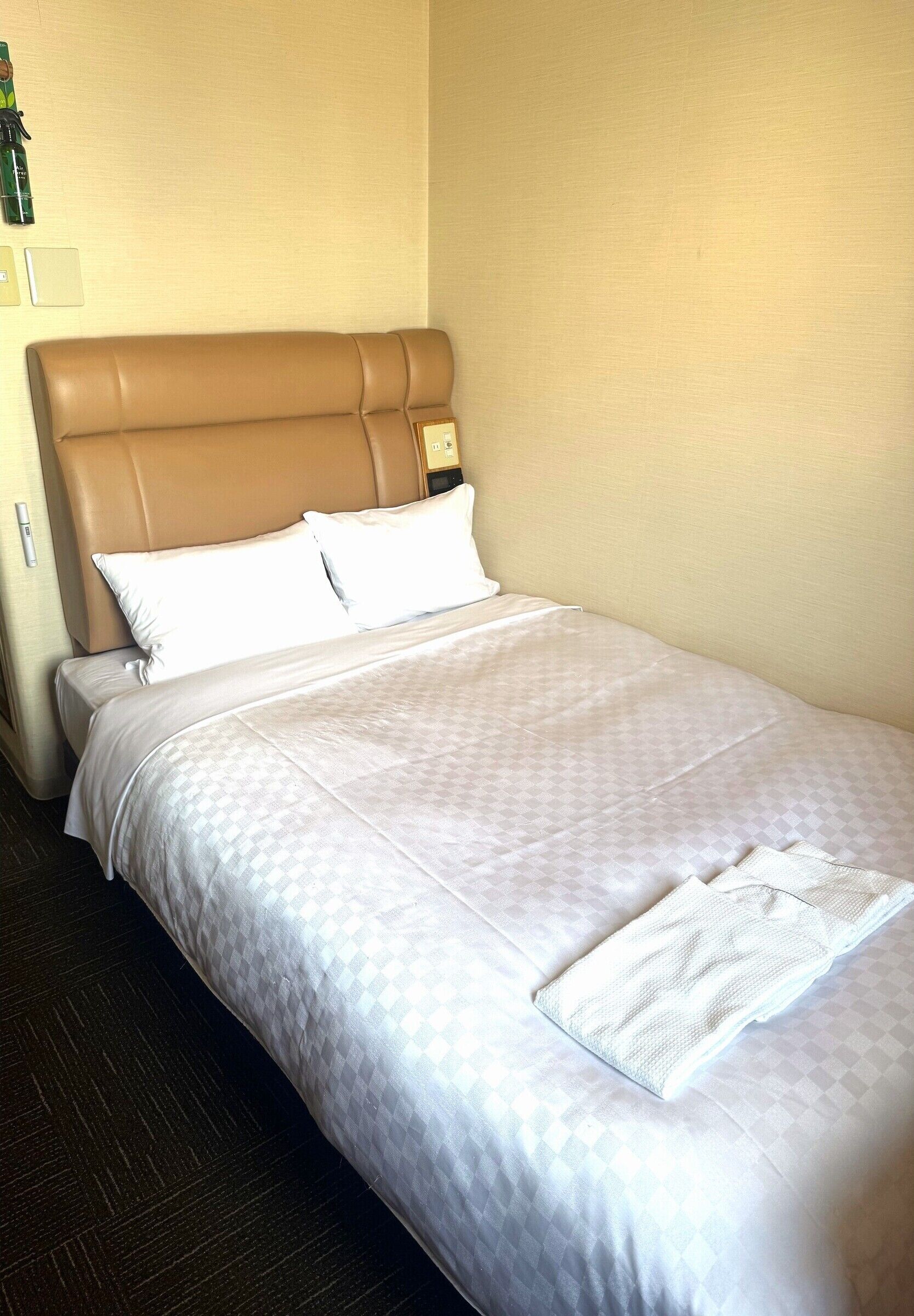Cama bem arrumada com cabeceira, roupa de cama branca e uma toalha dobrada sobre a cama.