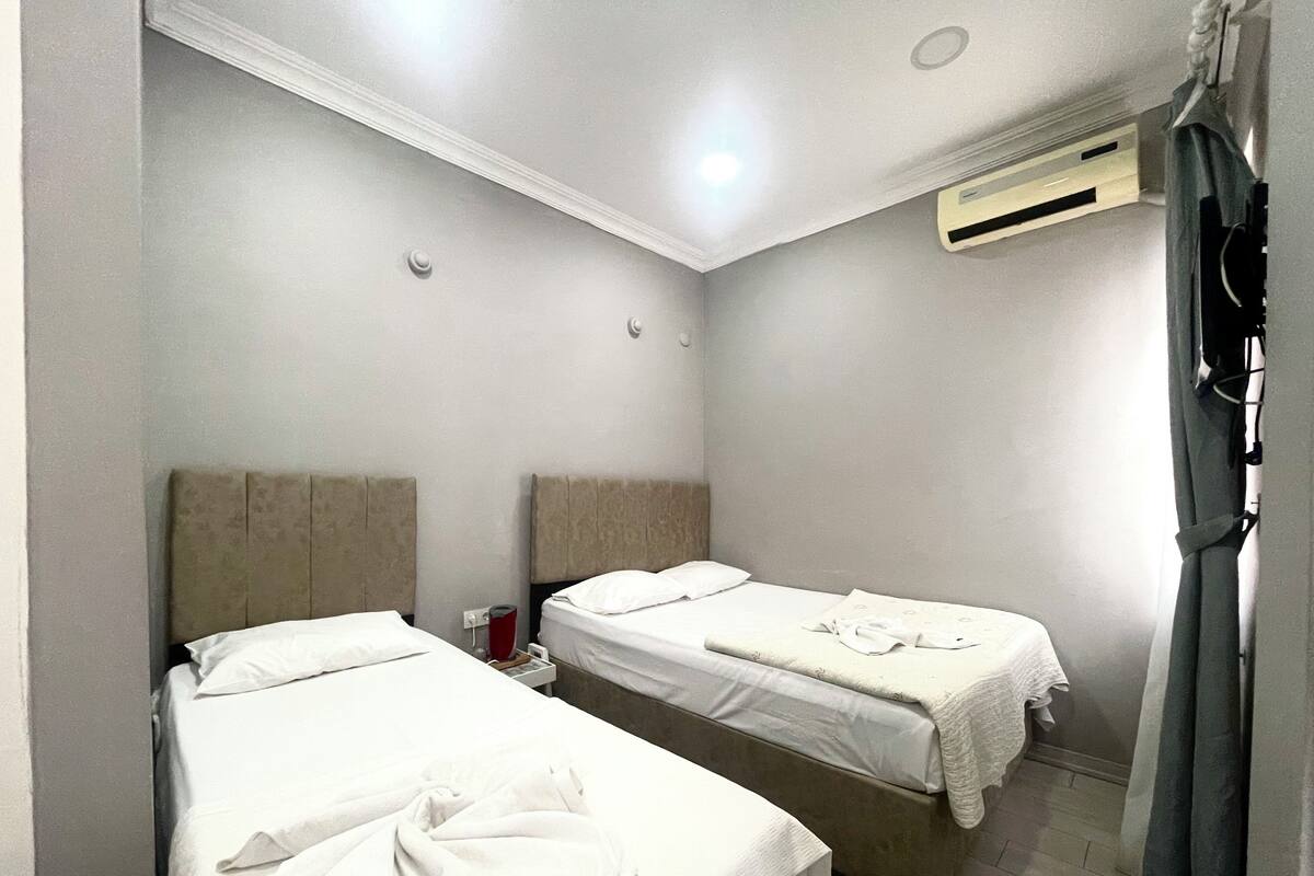 Hotellihuone, jossa on kaksi sänkyä, kattovalaisin, ilmastointilaite ja verho.