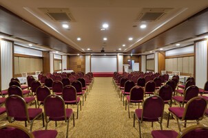 Un salón de conferencias con filas de sillas, una pantalla para proyector y un atril.