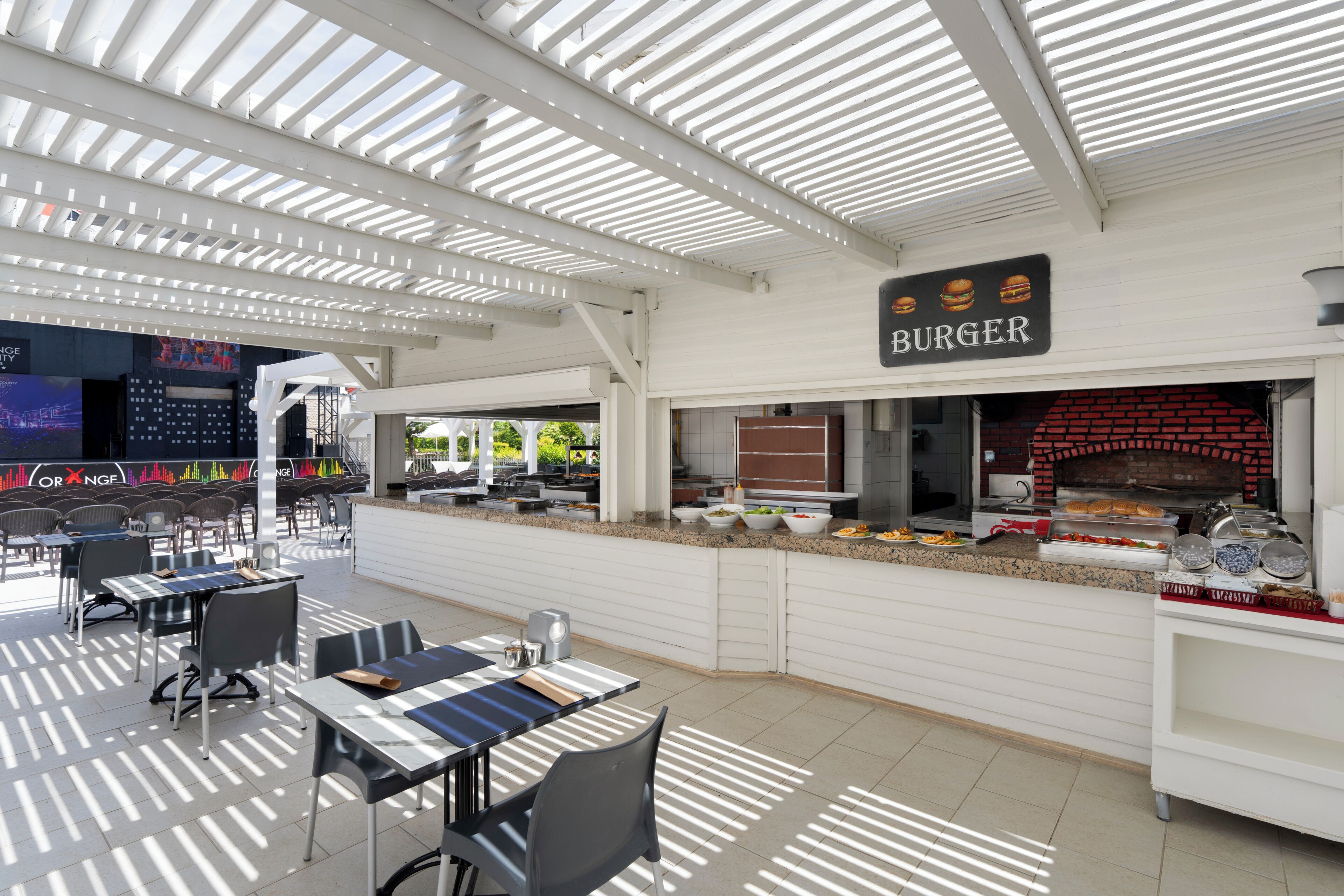 An outdoor dining area with tables and chairs, a brick oven, and a sign indicating a burger restaurant.