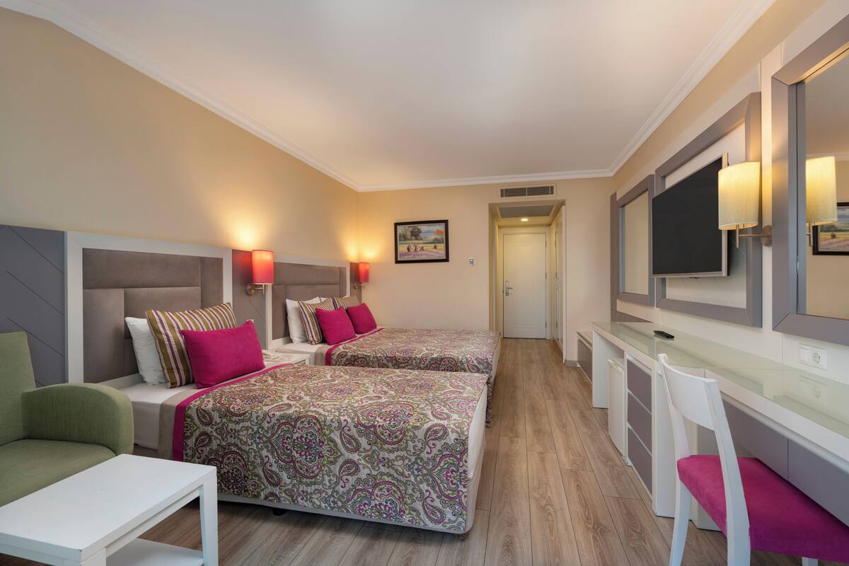 A hotel room with two beds, a desk, a chair, a TV, and a painting on the wall.