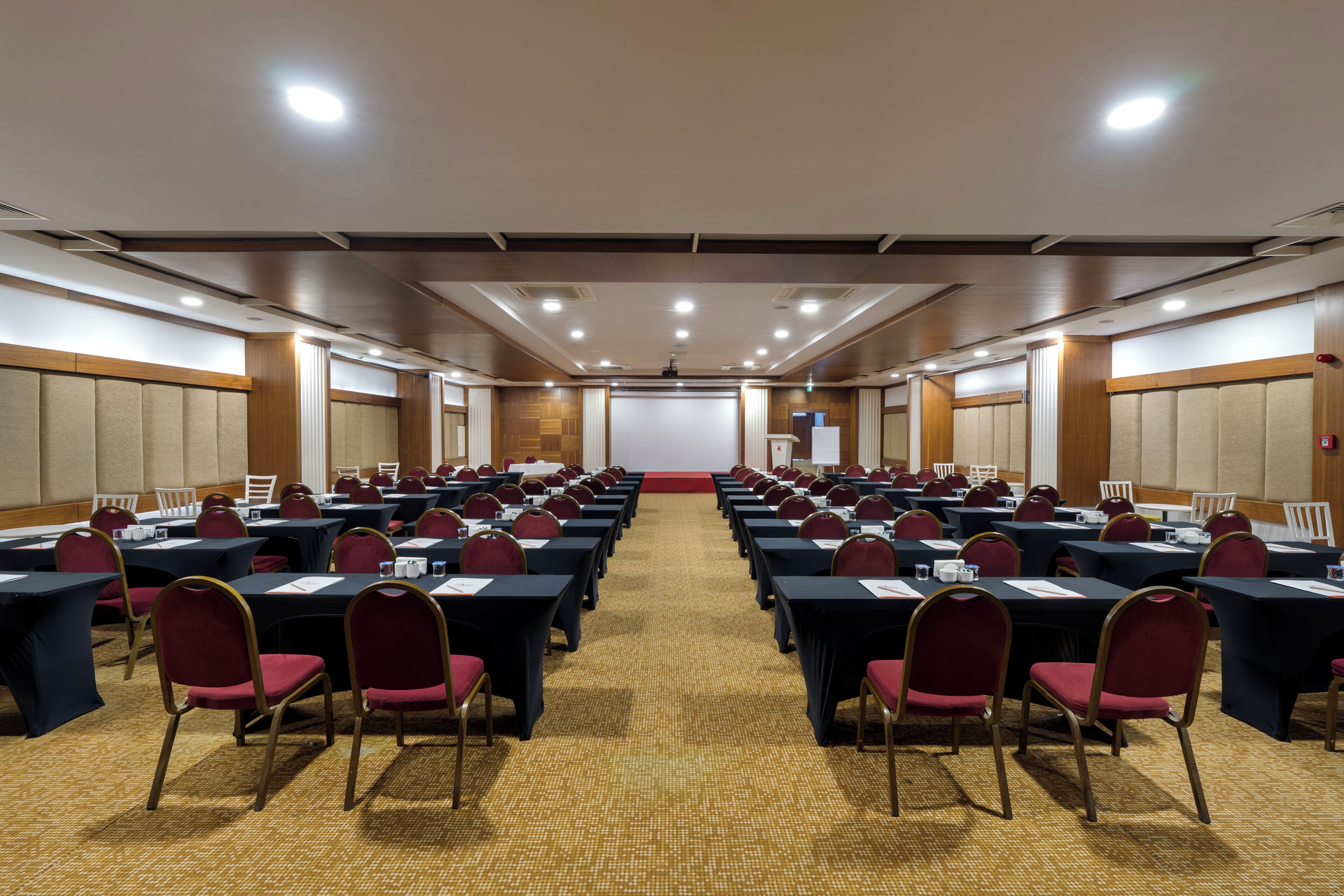 Una sala de conferencias con filas de mesas y sillas, un atril y suelo alfombrado.