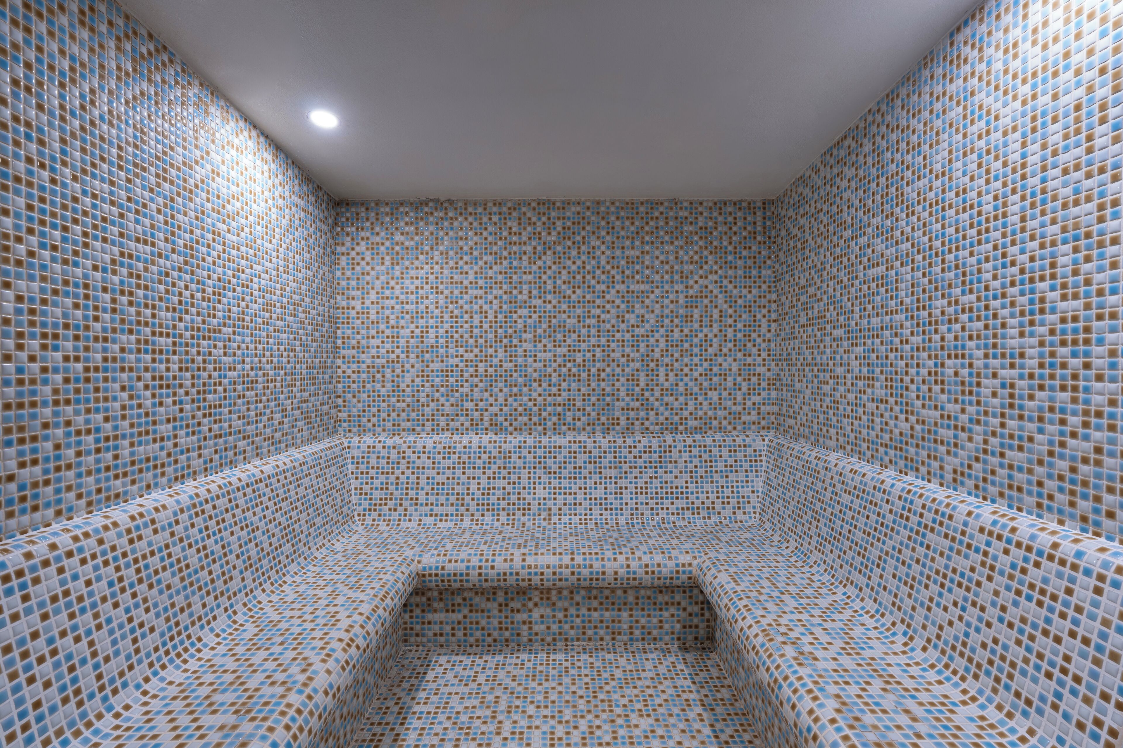 A room with a patterned tiled floor and walls, a flat ceiling, and a recessed light.