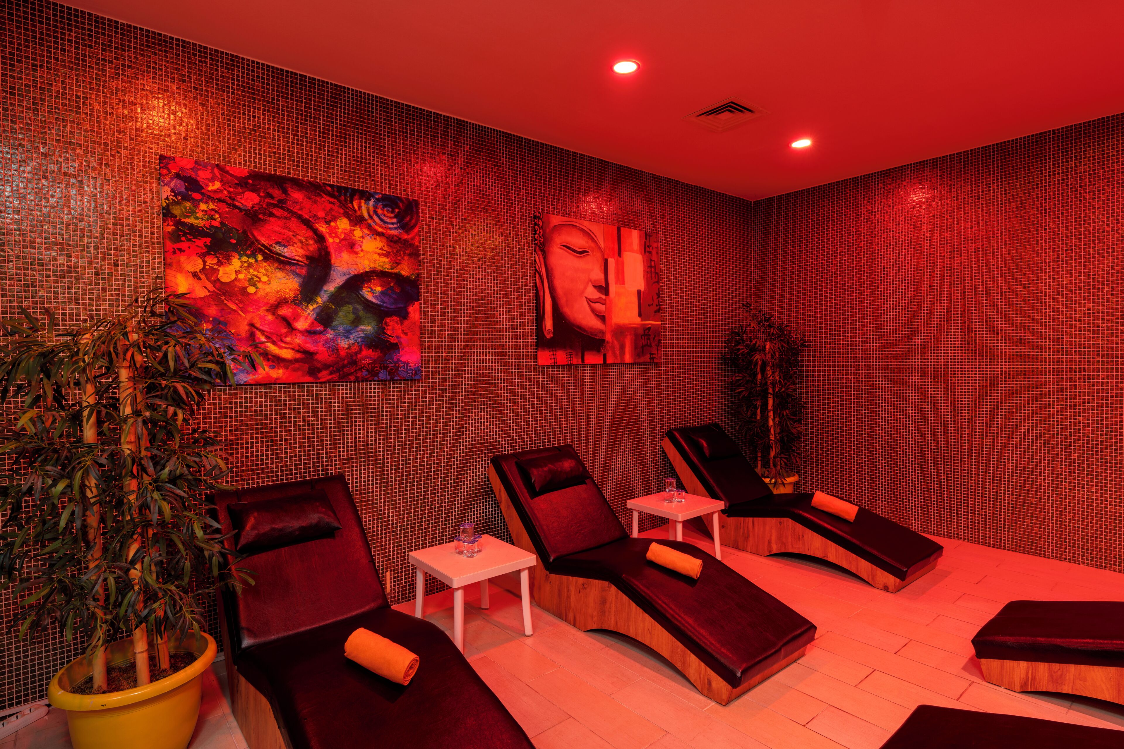 A spa room with massage chairs, a large abstract painting, a Buddha statue, and a potted plant.
